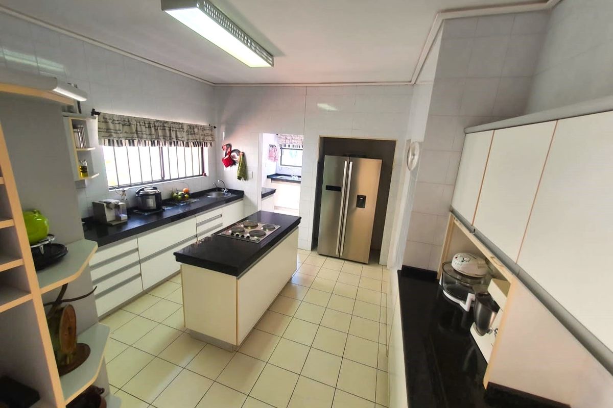 Spacious kitchen featuring a central island with a built-in cooktop, dark stone countertops, ample cabinetry, and an adjacent scullery area.