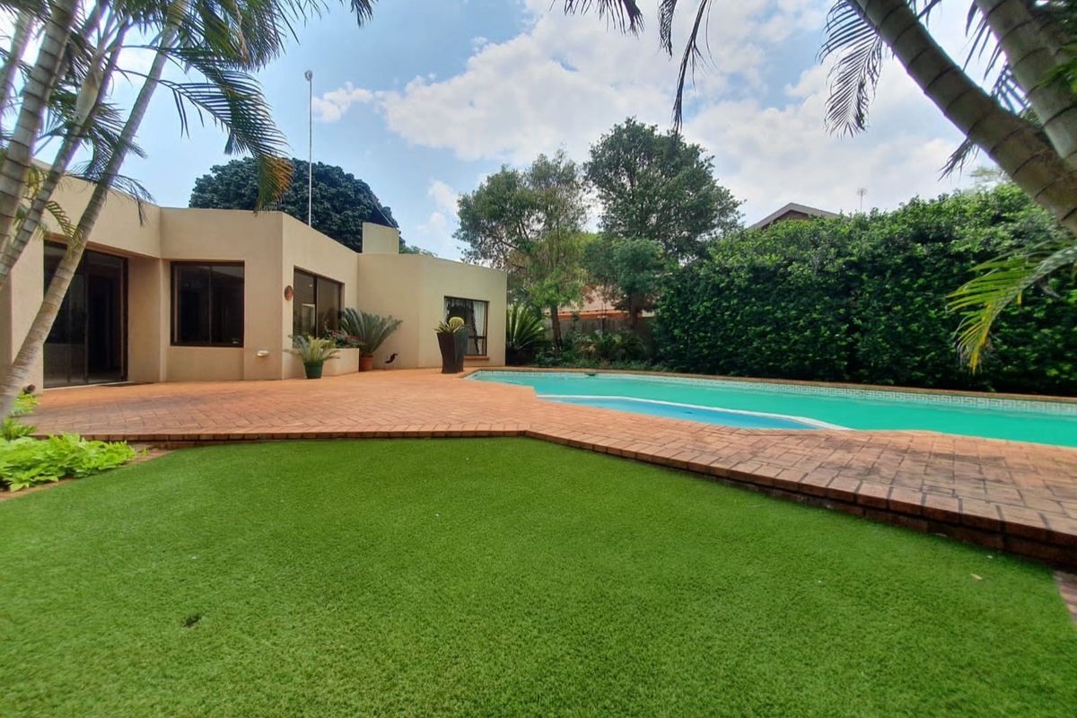 A spacious rear garden featuring a swimming pool, brick-paved patio area, and well-maintained artificial lawn, perfect for outdoor entertaining.