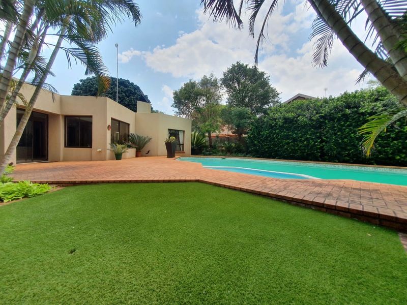 A spacious rear garden featuring a swimming pool, brick-paved patio area, and well-maintained artificial lawn, perfect for outdoor entertaining.