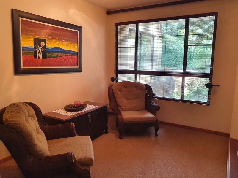 A cozy living area featuring large windows with fitted blinds, providing natural light and a view of the outdoor garden space.