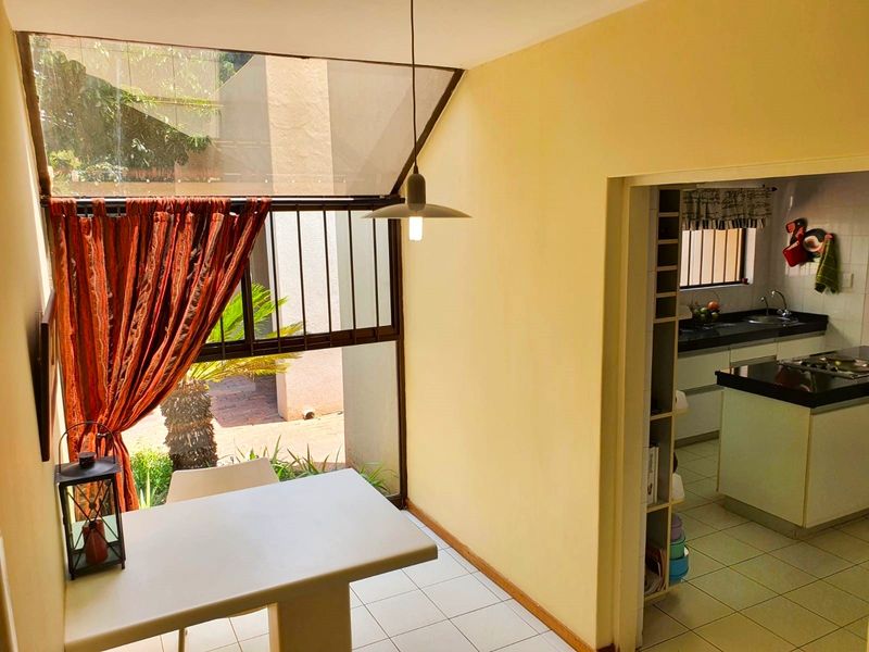 A bright dining area featuring large windows with security bars, adjacent to a functional kitchen with built-in cabinetry and stone countertops.