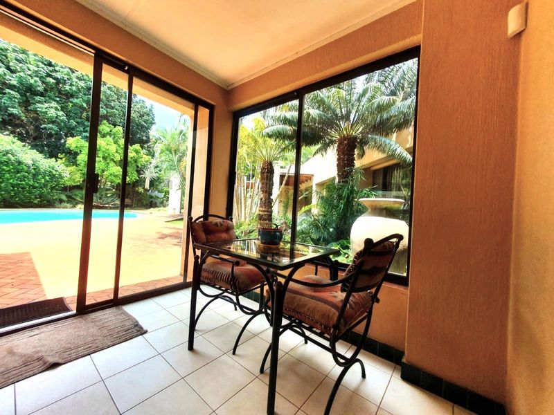 A sunroom or enclosed patio featuring large sliding glass doors, tiled flooring, and direct views of the garden and swimming pool area.