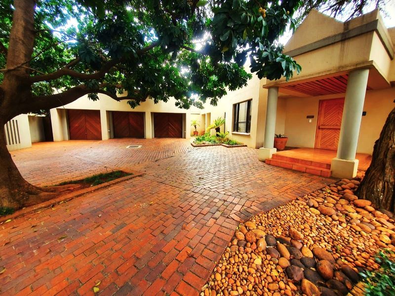 A spacious front entrance featuring a brick-paved driveway, triple garage doors, and a covered porch with structural columns.