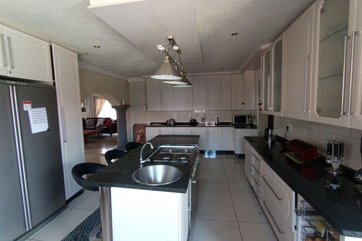 Spacious kitchen featuring a central island with a built-in hob and sink, granite countertops, and ample white cabinetry.