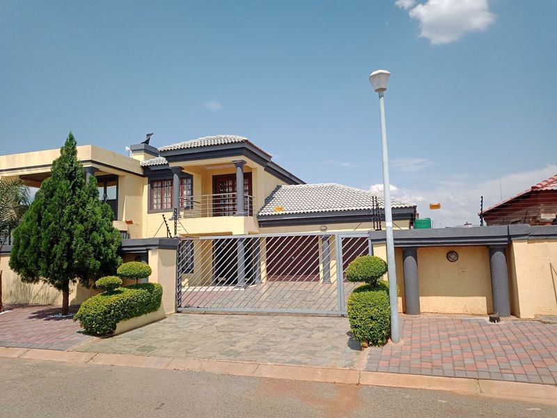 A two-story residential house featuring a gated entrance, paved driveway, balcony, and perimeter wall with integrated security fencing.