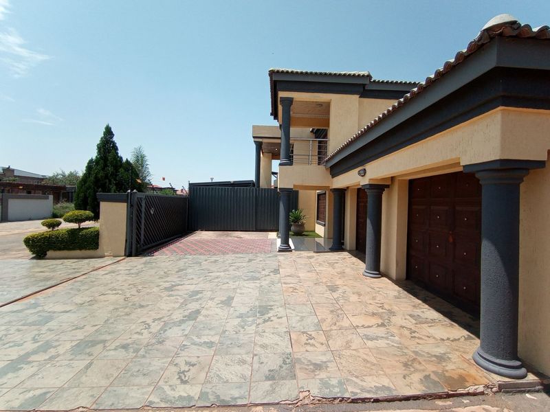 A well-maintained exterior front view featuring a paved driveway, double garage, decorative columns, and a secure gated entrance.