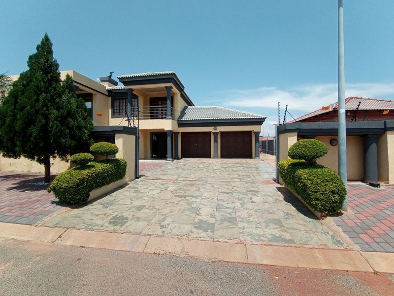 Front elevation of a double-story house featuring a paved driveway, double garage, and a balcony with decorative columns.