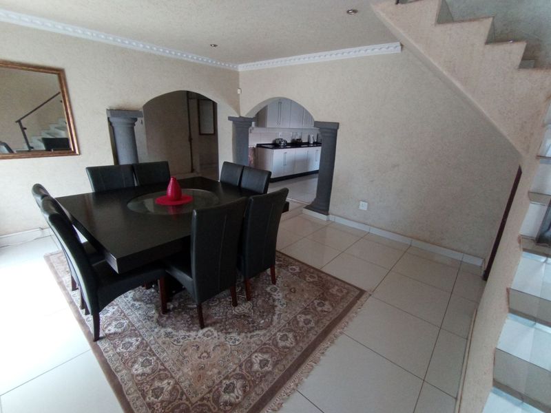Open plan dining area featuring tiled flooring, decorative archways with columns, and an adjacent kitchen view, with a staircase leading to the upper level.