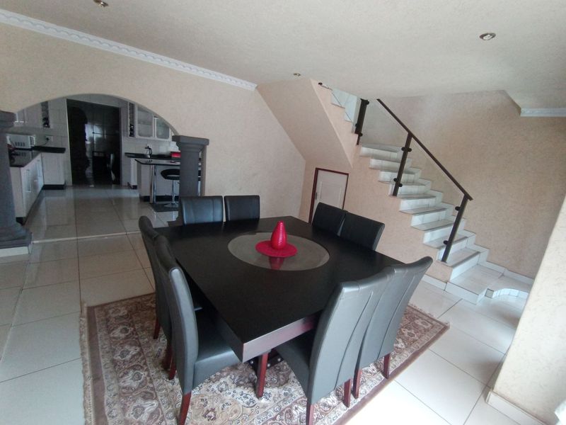 Open plan dining area featuring tiled flooring, a staircase with a metal balustrade, and an arched entryway leading into the kitchen.