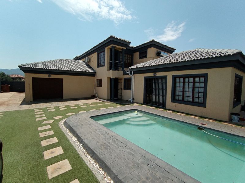 Rear view of the house featuring a swimming pool, paved surround, artificial lawn, and a double garage.