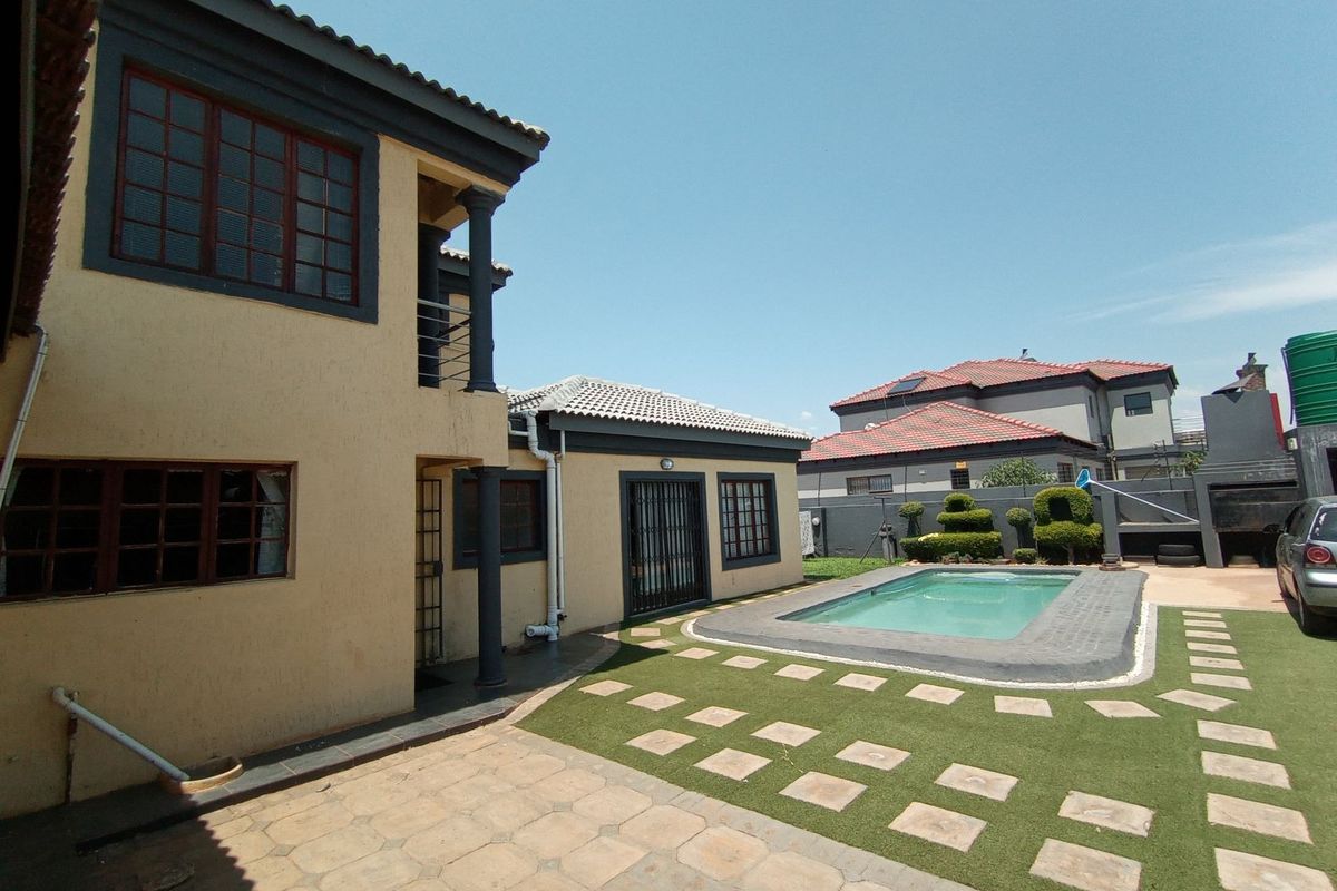 Rear exterior view featuring a swimming pool, paved patio area, artificial lawn, and two-story residential building structure.