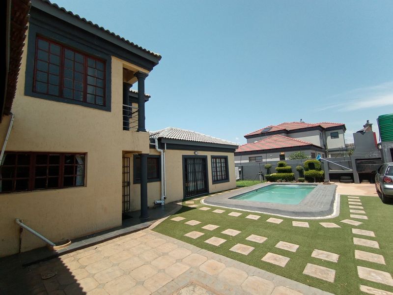 Rear exterior view featuring a swimming pool, paved patio area, artificial lawn, and two-story residential building structure.