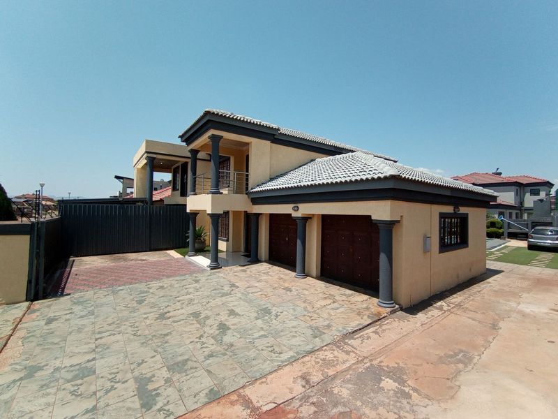 A double-story residential property featuring a paved driveway, double garage, and a covered balcony supported by decorative columns.