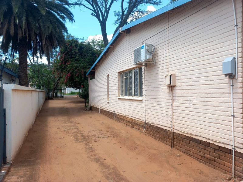 Side exterior view of the house featuring a painted brick facade, metal-framed windows, and an external air conditioning unit.