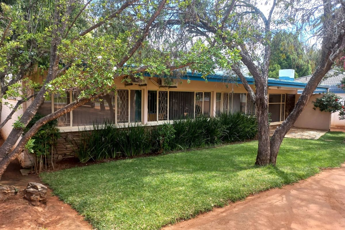 A view of the rear exterior of the house featuring a lawn, mature trees, and a paved patio area.