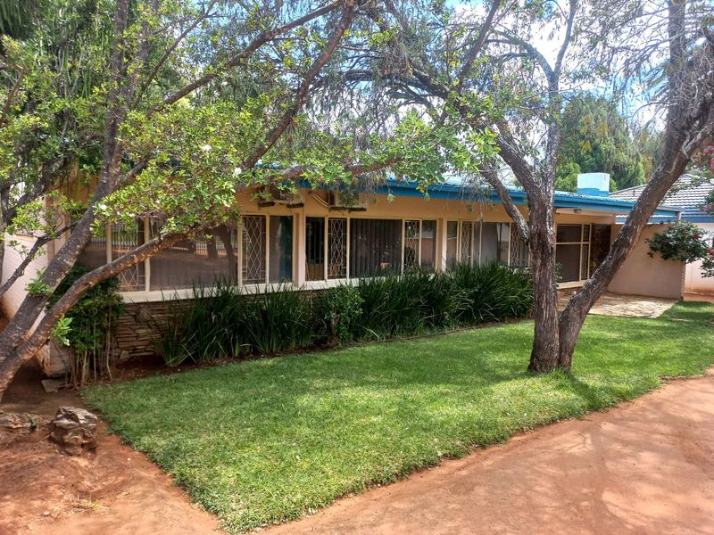 A view of the rear exterior of the house featuring a lawn, mature trees, and a paved patio area.