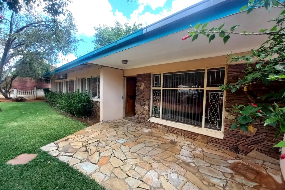 A covered patio area featuring natural stone paving and stone-clad exterior walls, overlooking a well-maintained garden space.