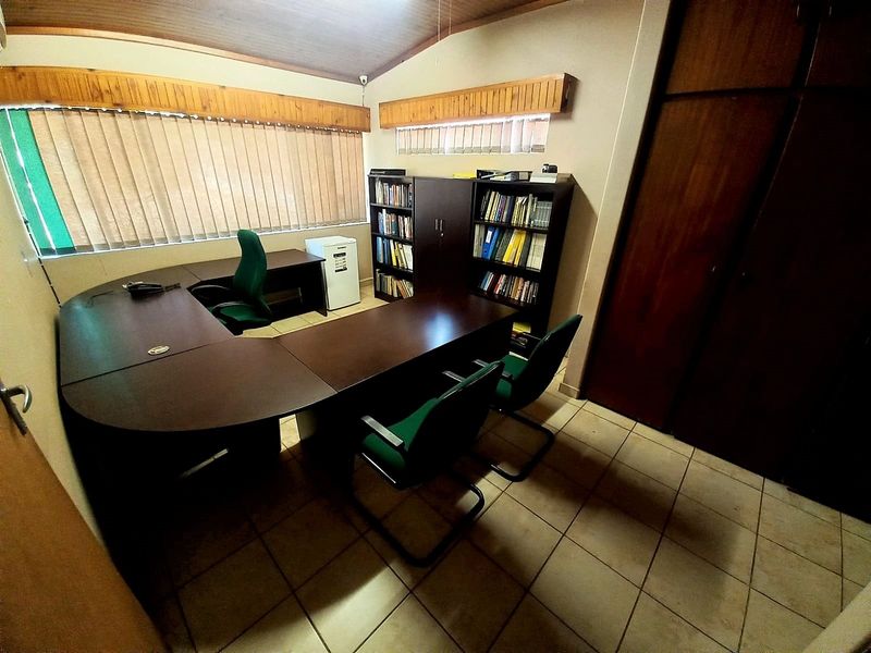 A functional home office featuring tiled flooring, built-in wooden cabinetry, and a vaulted timber-paneled ceiling with vertical blinds.