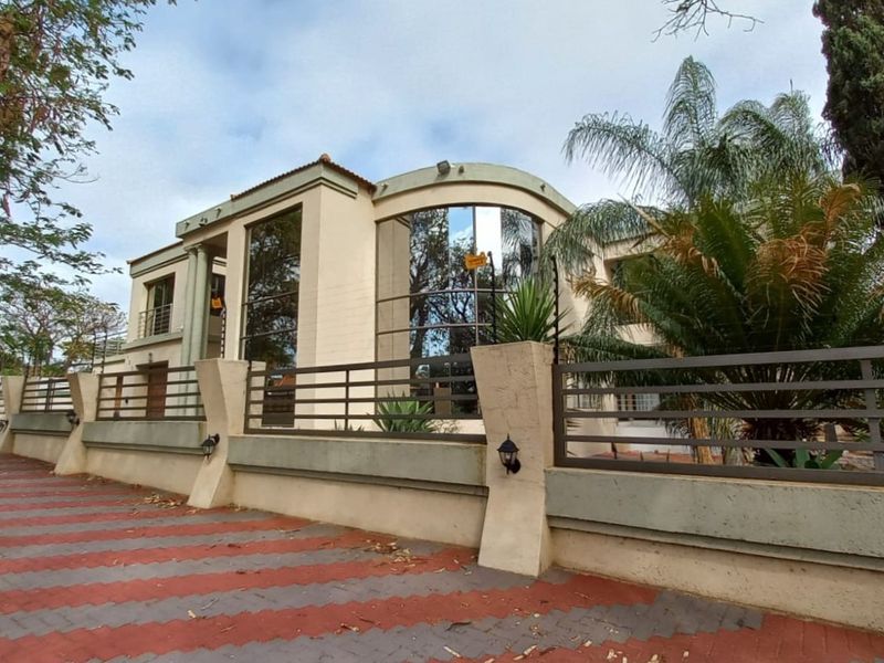 A modern two-story residence featuring a curved glass facade, paved driveway, and secure perimeter walling with integrated lighting.