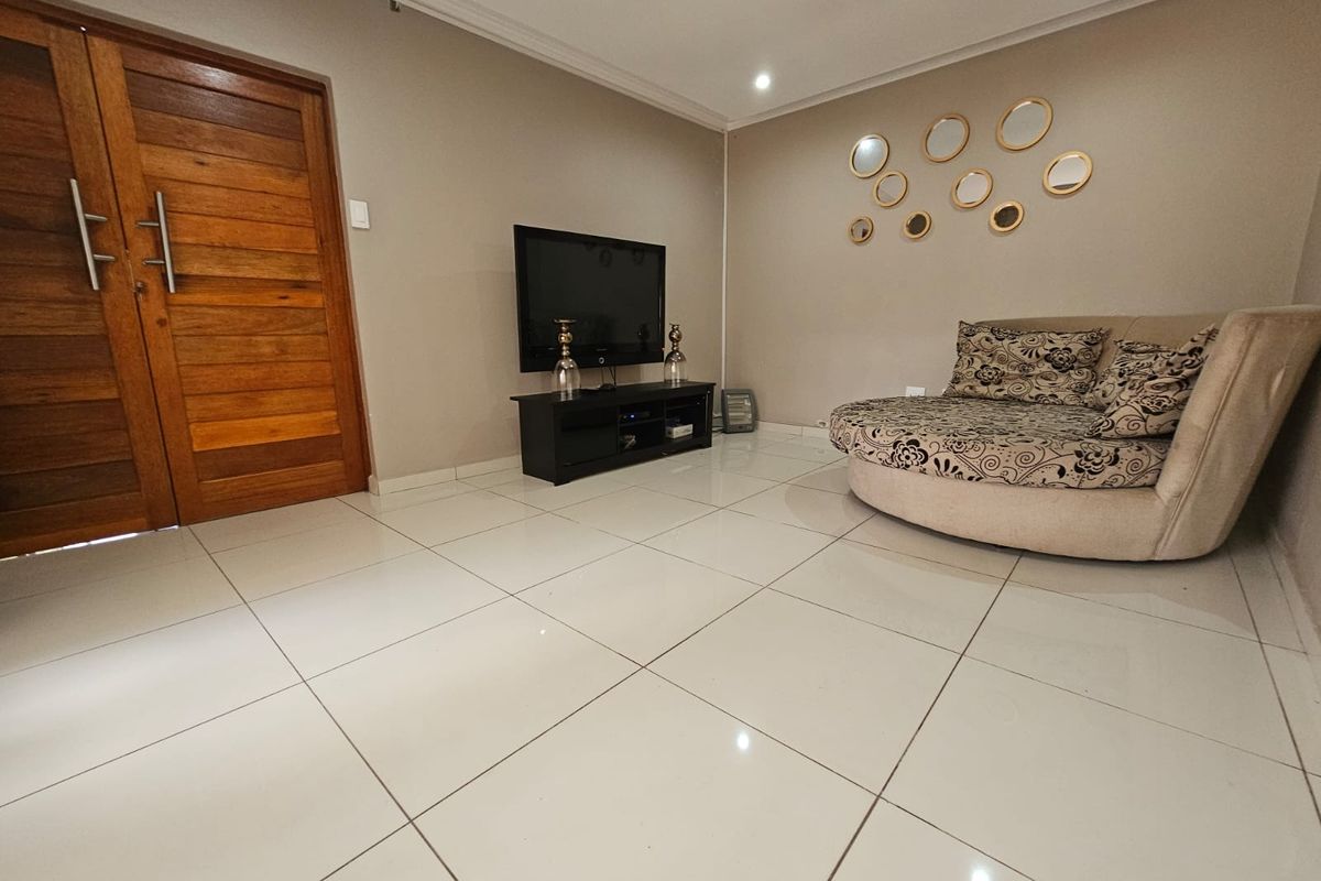 A bright living room featuring large format white floor tiles, recessed ceiling lighting, and a solid timber double door entrance.