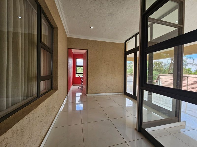 A bright, tiled sunroom or enclosed patio area featuring large glass windows and doors, providing access to an adjacent room and outdoor space.