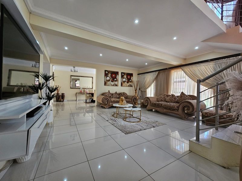 Spacious open-plan living area featuring polished porcelain floor tiles, recessed downlighting, and a modern staircase with stainless steel balustrades.