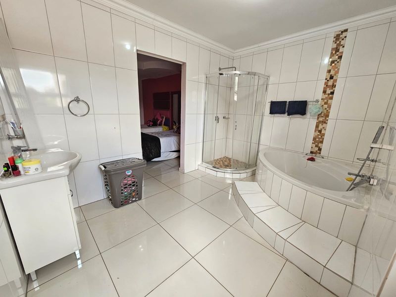 Spacious bathroom featuring a corner bathtub, separate glass-enclosed shower, and vanity basin with full-height wall tiling.