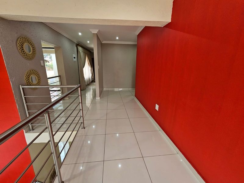 A bright hallway featuring polished porcelain floor tiles, recessed ceiling lighting, and a modern stainless steel balustrade overlooking the lower level.