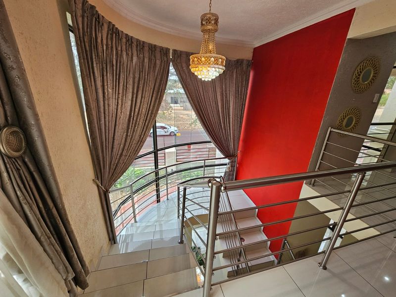 A bright staircase area featuring tiled steps, a modern stainless steel balustrade, and a large curved window with a decorative chandelier.
