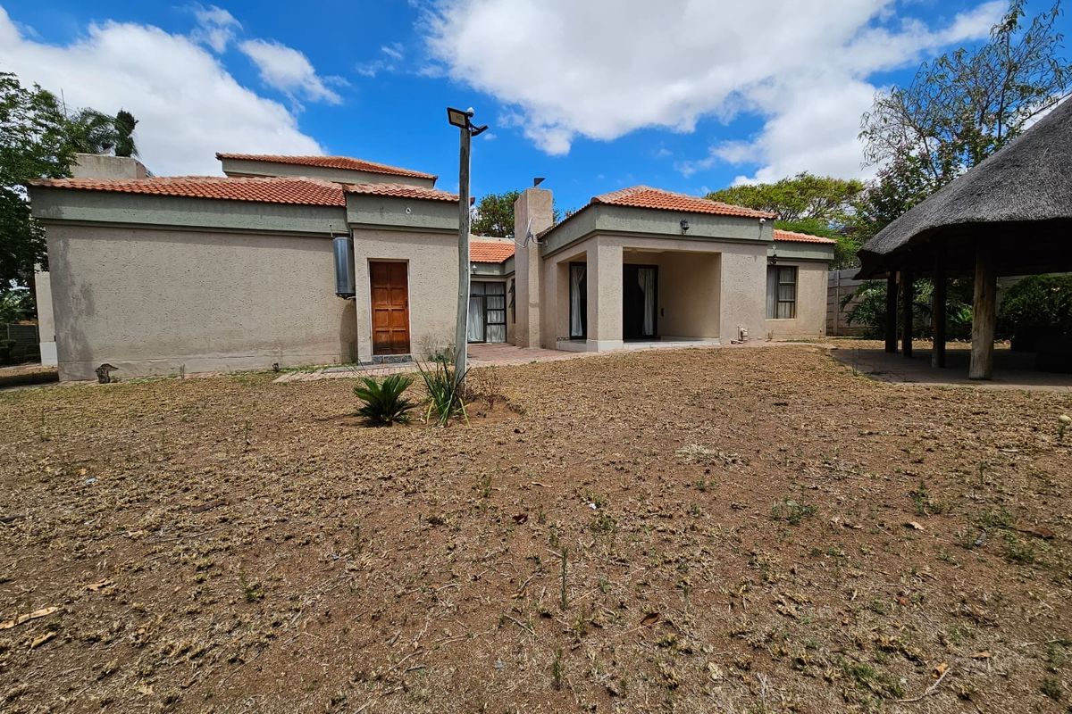 Rear view of the house featuring a patio area, tiled roof, and a large garden space with a thatched lapa structure.