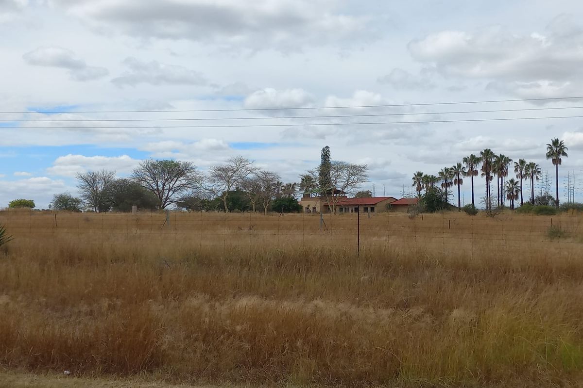 A wide-angle view of a farm property featuring a main dwelling set back from the road, surrounded by open fields and mature trees.