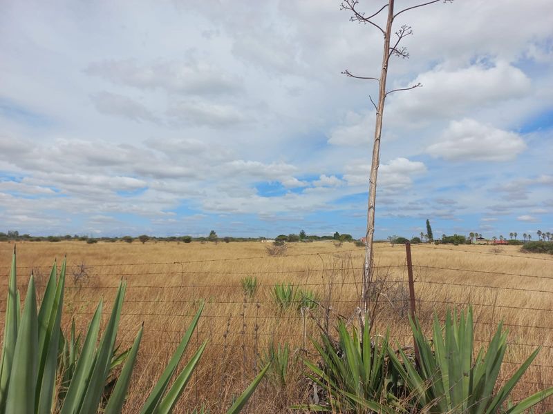 Expansive open farm land featuring dry grass, native vegetation, and perimeter wire fencing under a cloudy sky.