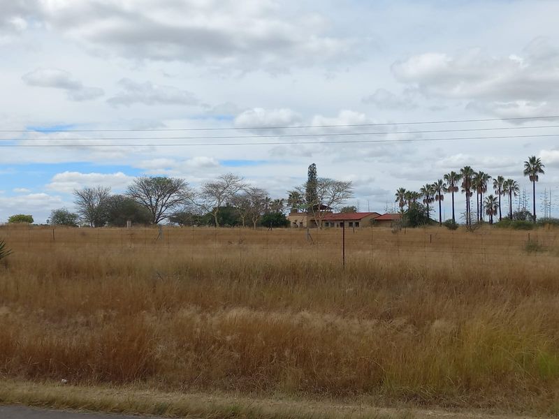 A wide-angle view of a farm property featuring a main dwelling set back from the road, surrounded by open fields and mature trees.