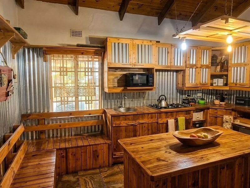 Rustic-style kitchen featuring corrugated metal wall cladding, extensive timber cabinetry, a central timber island, and exposed ceiling beams with integrated lighting.