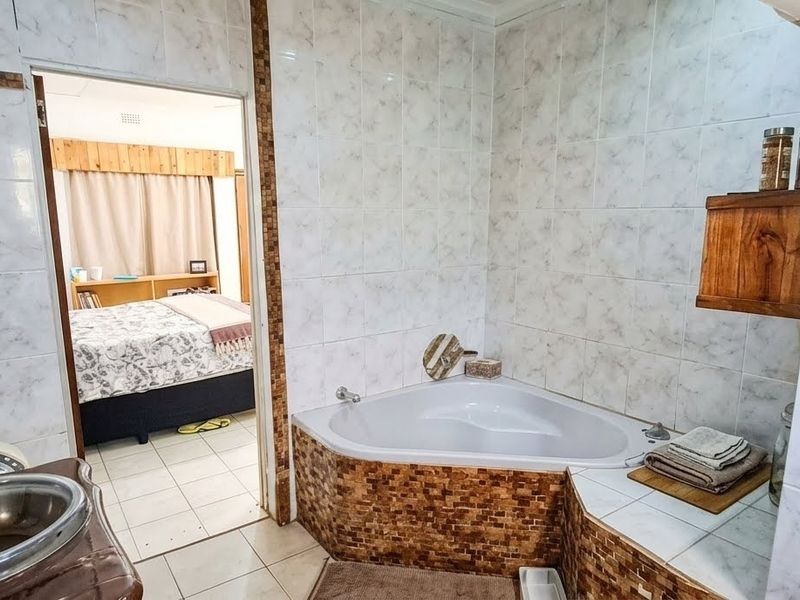 A bathroom featuring a corner bathtub with mosaic tile surround, a vessel sink vanity, and full-height wall tiling, with an adjacent bedroom view.