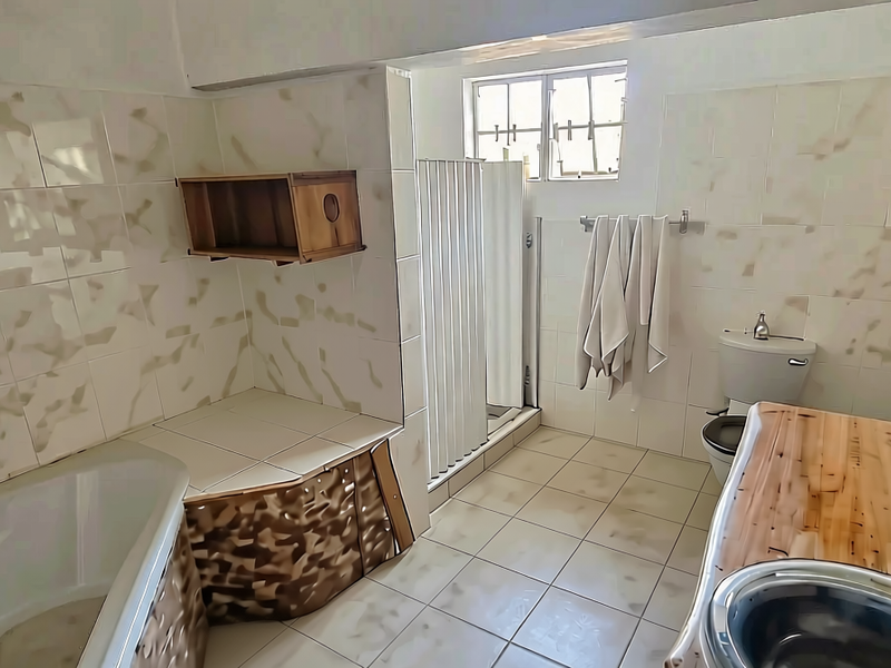A functional bathroom featuring a built-in bathtub, separate shower enclosure, toilet, and a vanity basin with a wooden countertop.