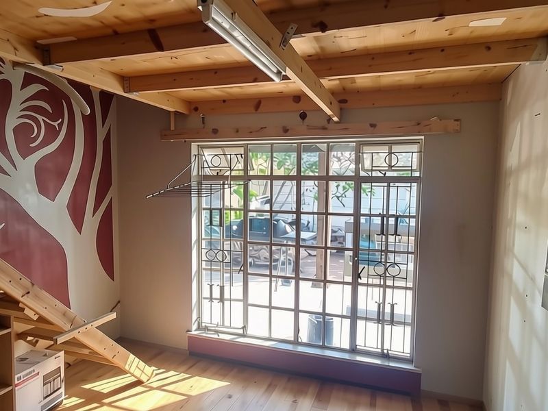 Living area featuring exposed timber ceiling beams, timber staircase, and large window with security gate, offering a rustic aesthetic with potential for refinement.