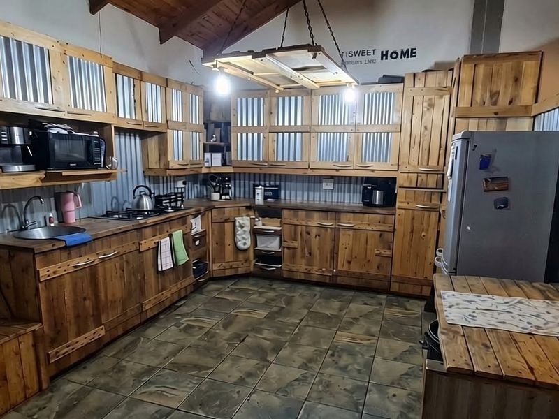 Rustic-style kitchen featuring timber cabinetry, corrugated metal splashbacks, tiled flooring, and exposed timber ceiling beams with integrated lighting.