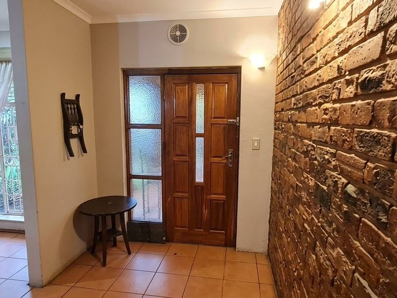 Entrance foyer featuring a rustic exposed brick wall, tiled flooring, and a solid timber front door with integrated glass side panels.