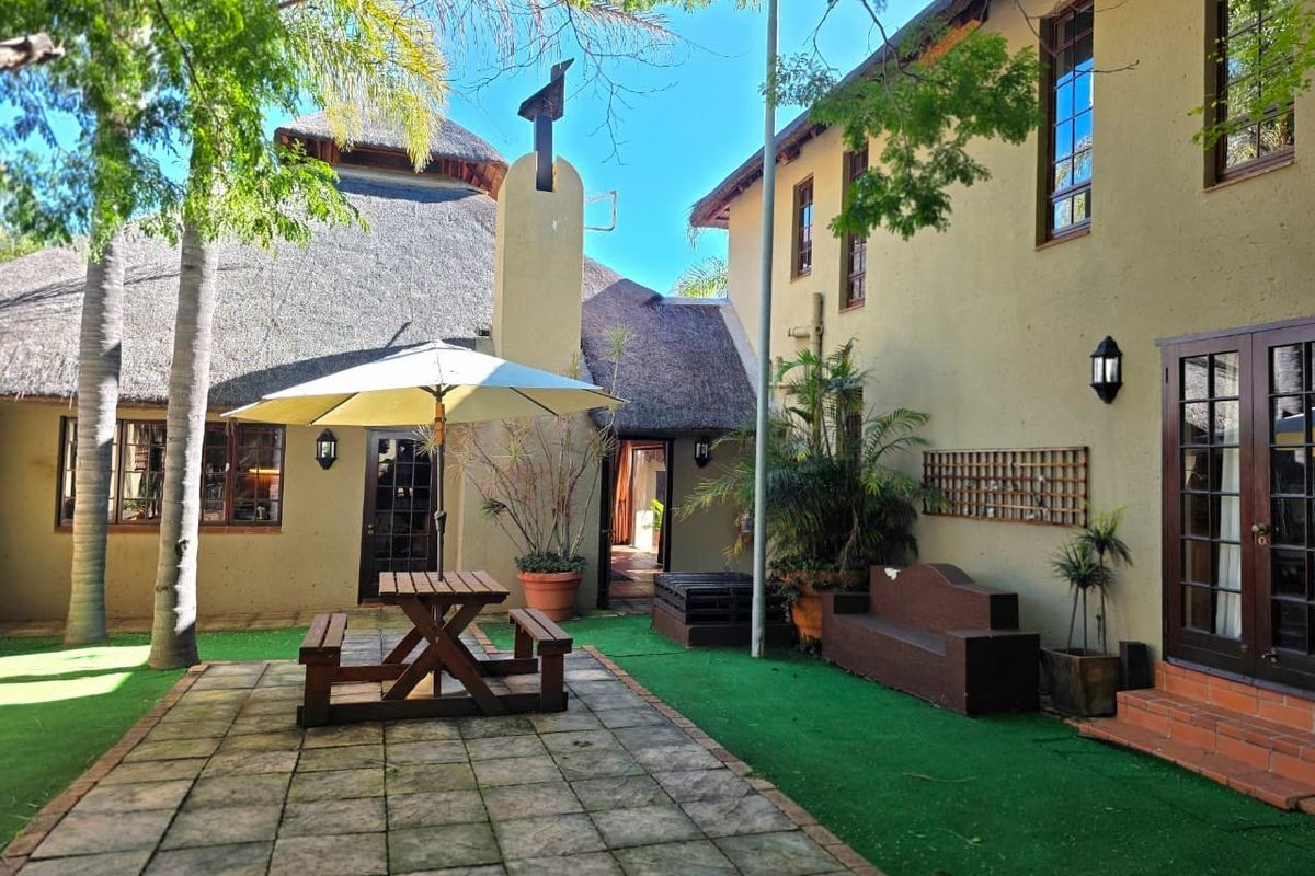 A private rear courtyard featuring a paved patio area, artificial lawn, and traditional thatched roof architecture with direct access to the home.