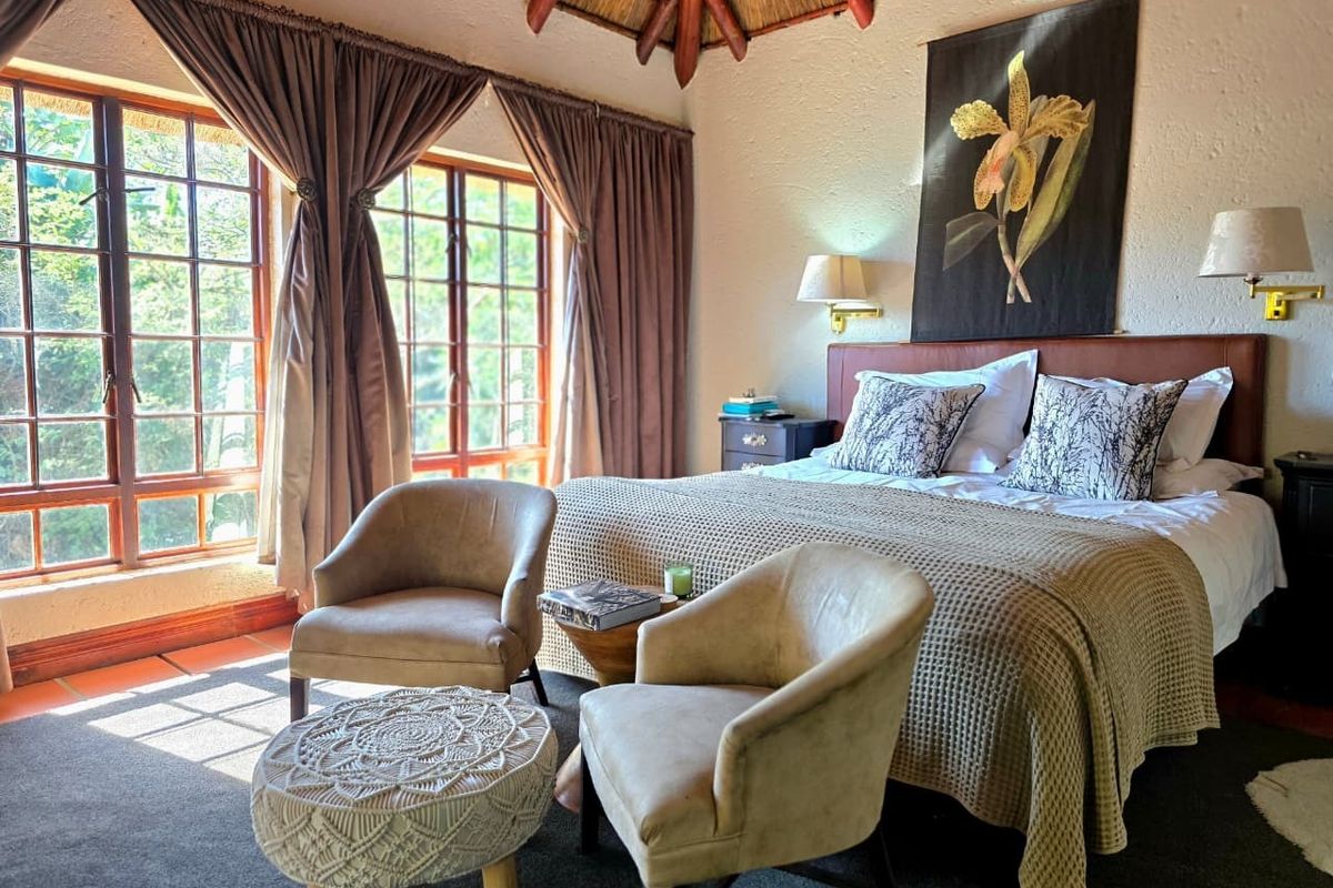 A cozy bedroom featuring a high thatched ceiling, large windows with natural light, and a warm, inviting atmosphere.