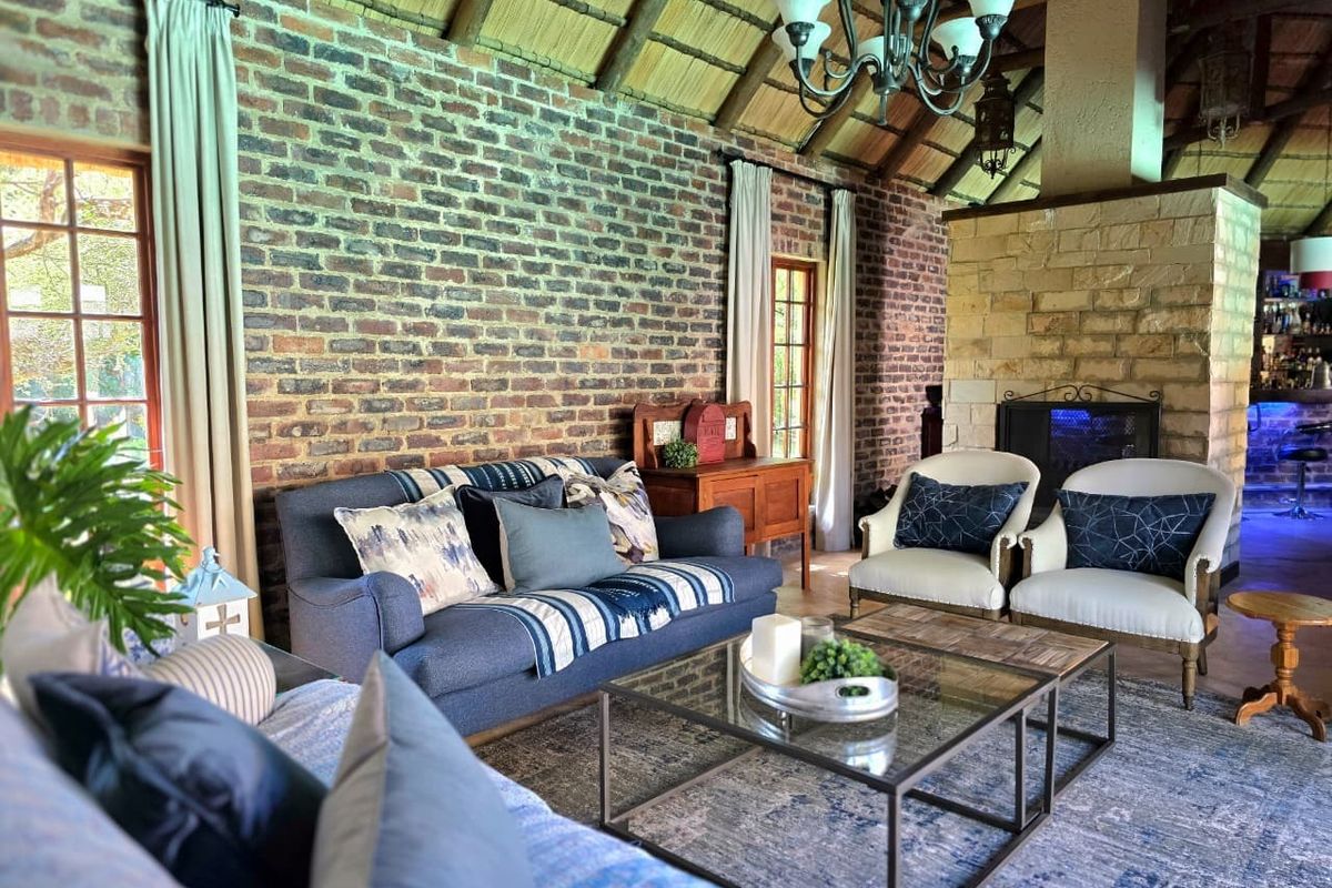 Spacious living room featuring a high thatched roof, exposed brick walls, and a prominent stone fireplace, creating a warm and rustic atmosphere.