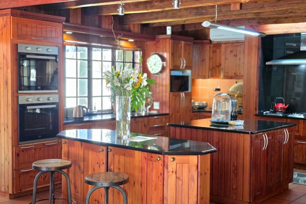 Spacious kitchen featuring extensive timber cabinetry, dual kitchen islands with dark stone countertops, built-in double ovens, and exposed timber ceiling beams.