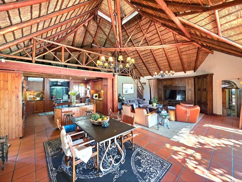 Spacious open-plan living area featuring a high vaulted thatched ceiling, exposed timber trusses, terracotta floor tiles, and a well-appointed wooden kitchen.