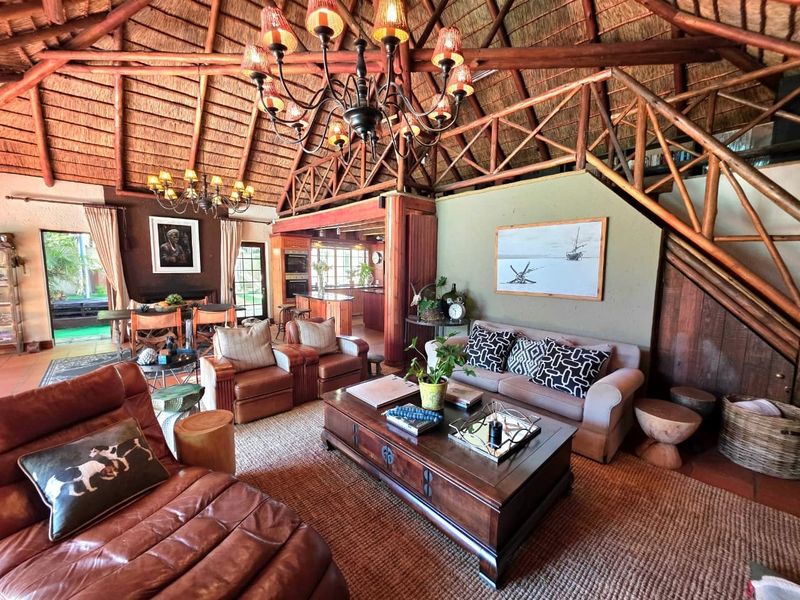 Spacious open-plan living area featuring a high vaulted thatched ceiling with exposed timber trusses, a grand chandelier, and seamless flow to the kitchen.