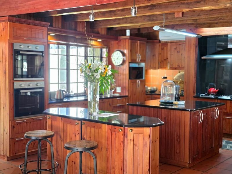 Spacious kitchen featuring extensive timber cabinetry, dual kitchen islands with dark stone countertops, built-in double ovens, and exposed timber ceiling beams.