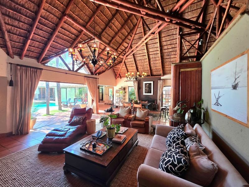Spacious open-plan living area featuring a high vaulted thatched ceiling, exposed timber beams, and large sliding doors opening onto a pool patio.