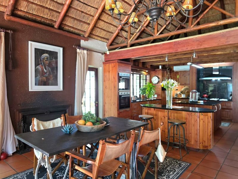 Open-plan living and kitchen area featuring a high thatched roof, exposed timber beams, built-in oven, and a central kitchen island with granite countertops.