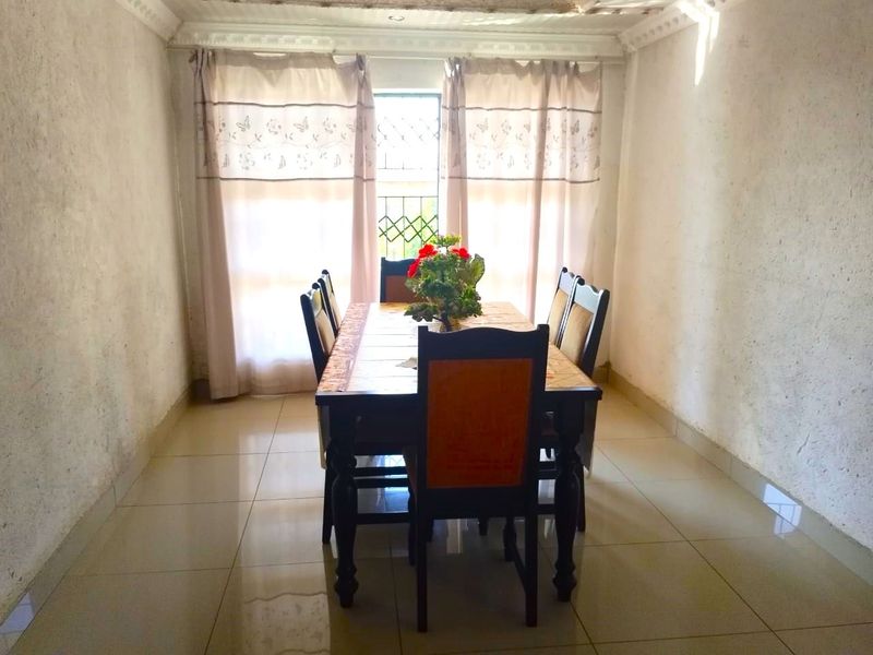 A dining room featuring tiled flooring, decorative ceiling cornicing, and a window with security bars, requiring cosmetic updates to the walls and ceiling.