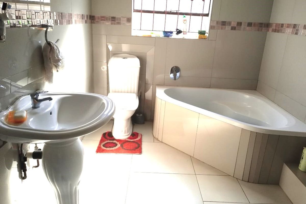 A functional bathroom featuring a corner bathtub, pedestal basin, and toilet with neutral wall and floor tiling.